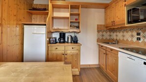 A kitchen with wooden cabinets, a white refrigerator, a coffee maker, a toaster, and a microwave. - 250m from ski slopes, 4th floor, balcony, 38m², Méribel-Mottaret (Méribel - Les Allues)