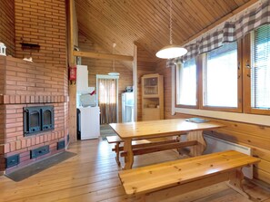 Un intérieur en bois avec une cheminée en briques, une table à manger avec des bancs et un coin cuisine.
