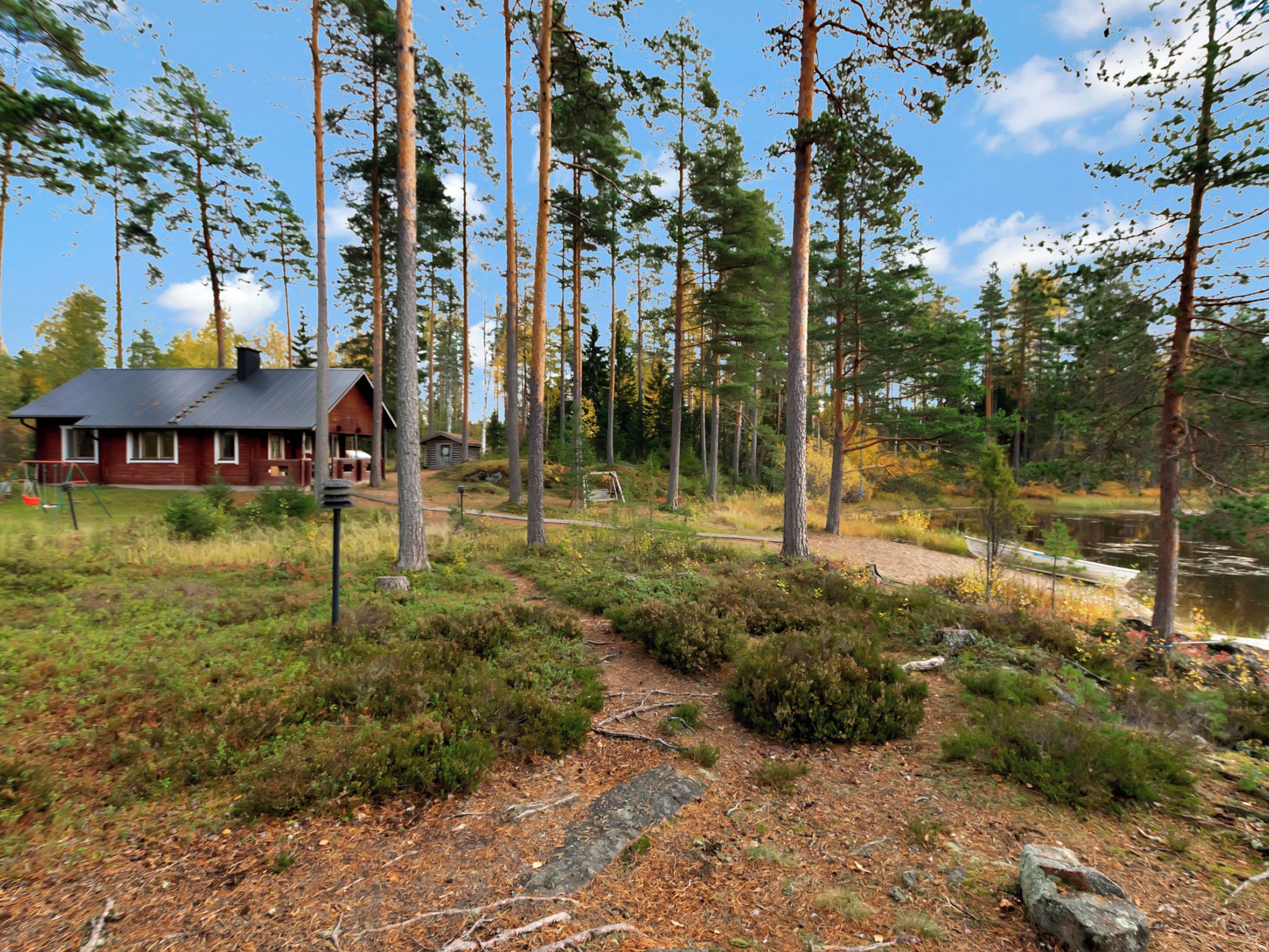 En stuga med ett tak av metall, omgiven av en skog och en liten sjö eller damm.