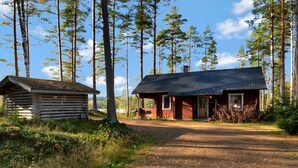 A cabin with a metal roof and a wooden structure nearby, surrounded by tall trees and a clear sky. - Kuusikumpu by Interhome (Petäjävesi)
