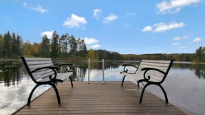 A wooden dock with two benches facing a calm lake, surrounded by trees and a clear sky. - Kuusikumpu by Interhome (Petäjävesi)