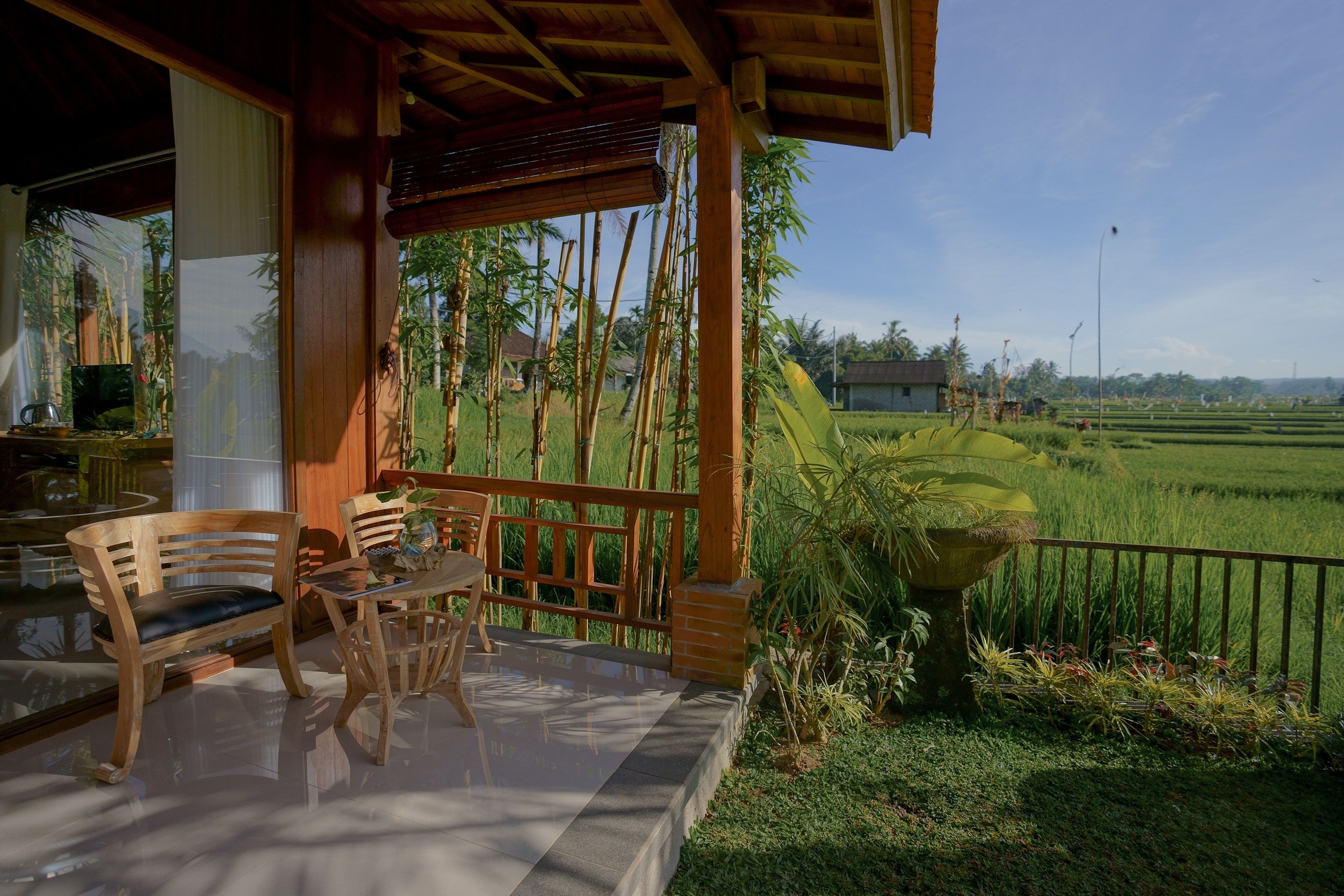 A wooden deck with a table and chairs, overlooking a lush green field and bamboo forest.
