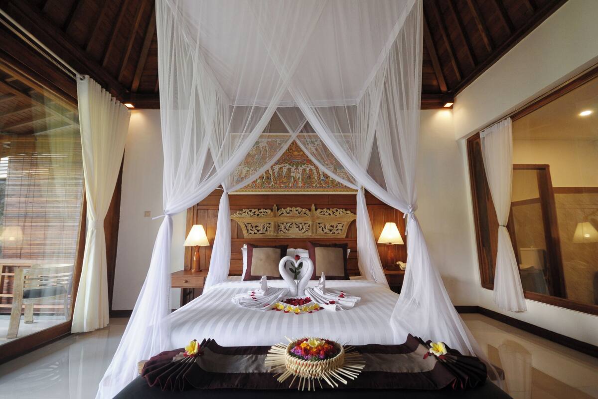 A four-poster bed with a canopy, a decorative headboard, and a floral arrangement on the bed.