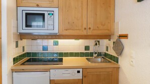 Una cocina compacta con armarios de madera, microondas, lavavajillas y pileta.