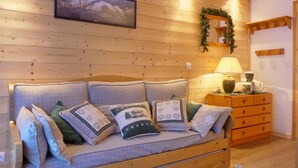 Una habitación acogedora con una pared de madera, un sofá con cojines estampados, una mesita auxiliar con una lámpara y un cuadro enmarcado sobre el sofá.