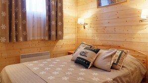 Una habitación acogedora de madera con una cama, una lámpara de pared y una ventana con cortinas.