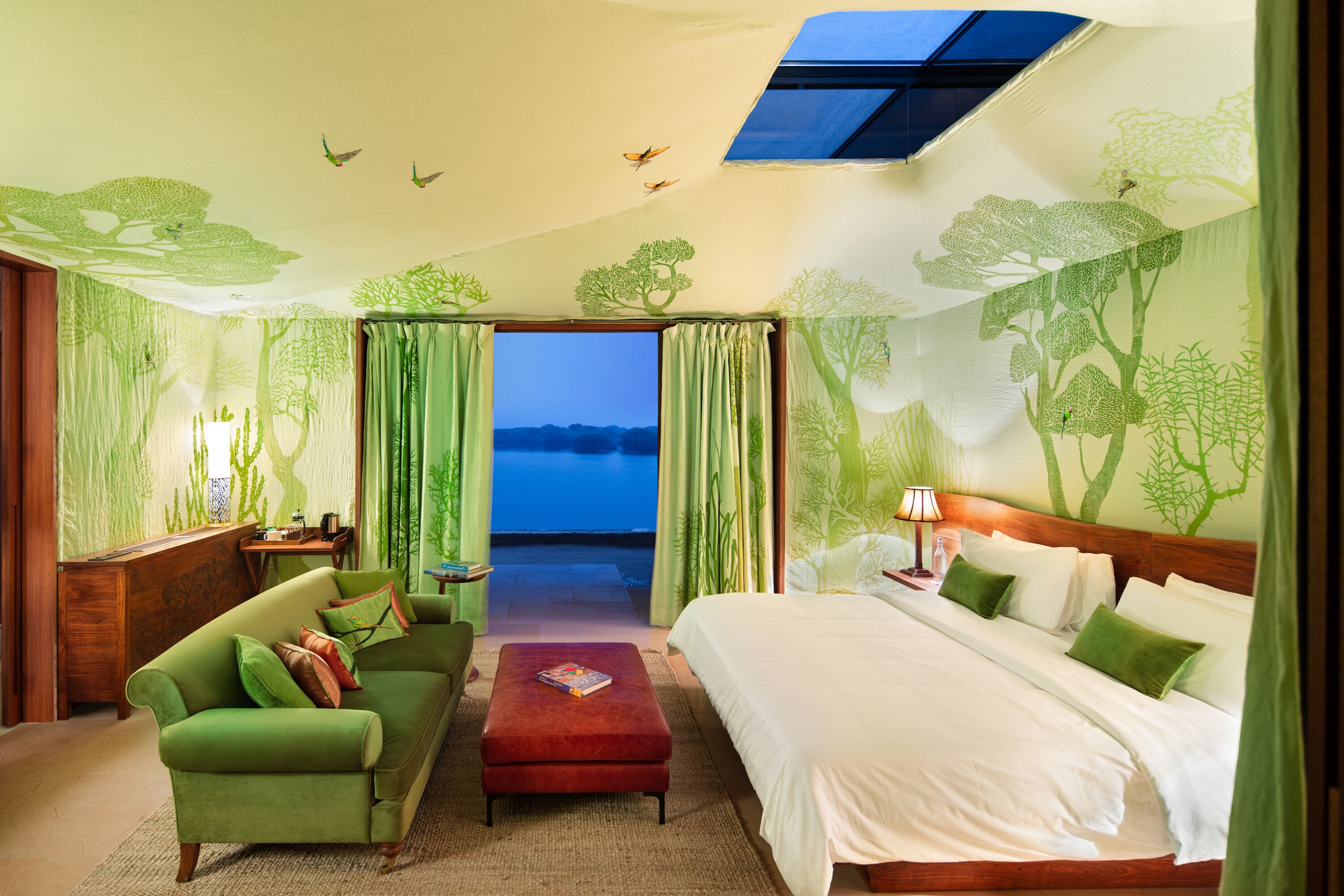 A hotel room with a large bed, a green sofa, a small table, and a view of the sea through the curtains.