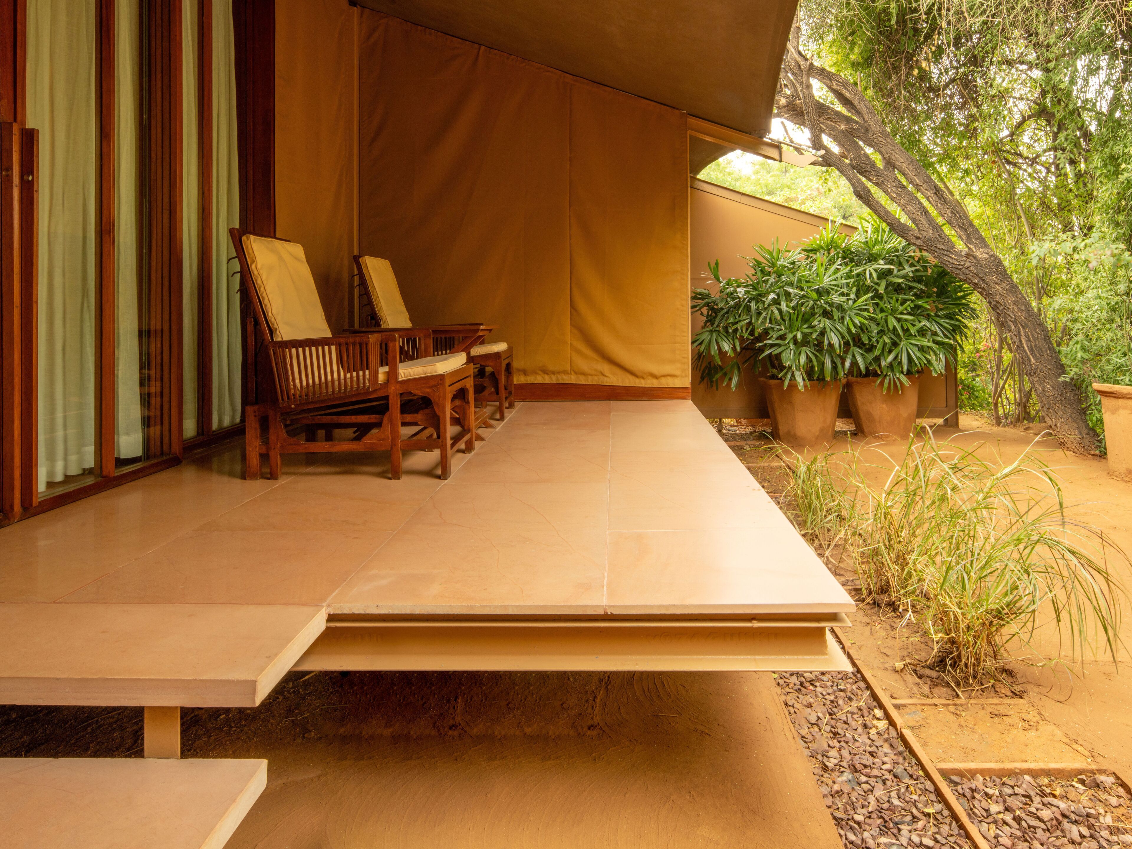 A covered outdoor seating area with wooden chairs and a table, surrounded by potted plants and a small garden.