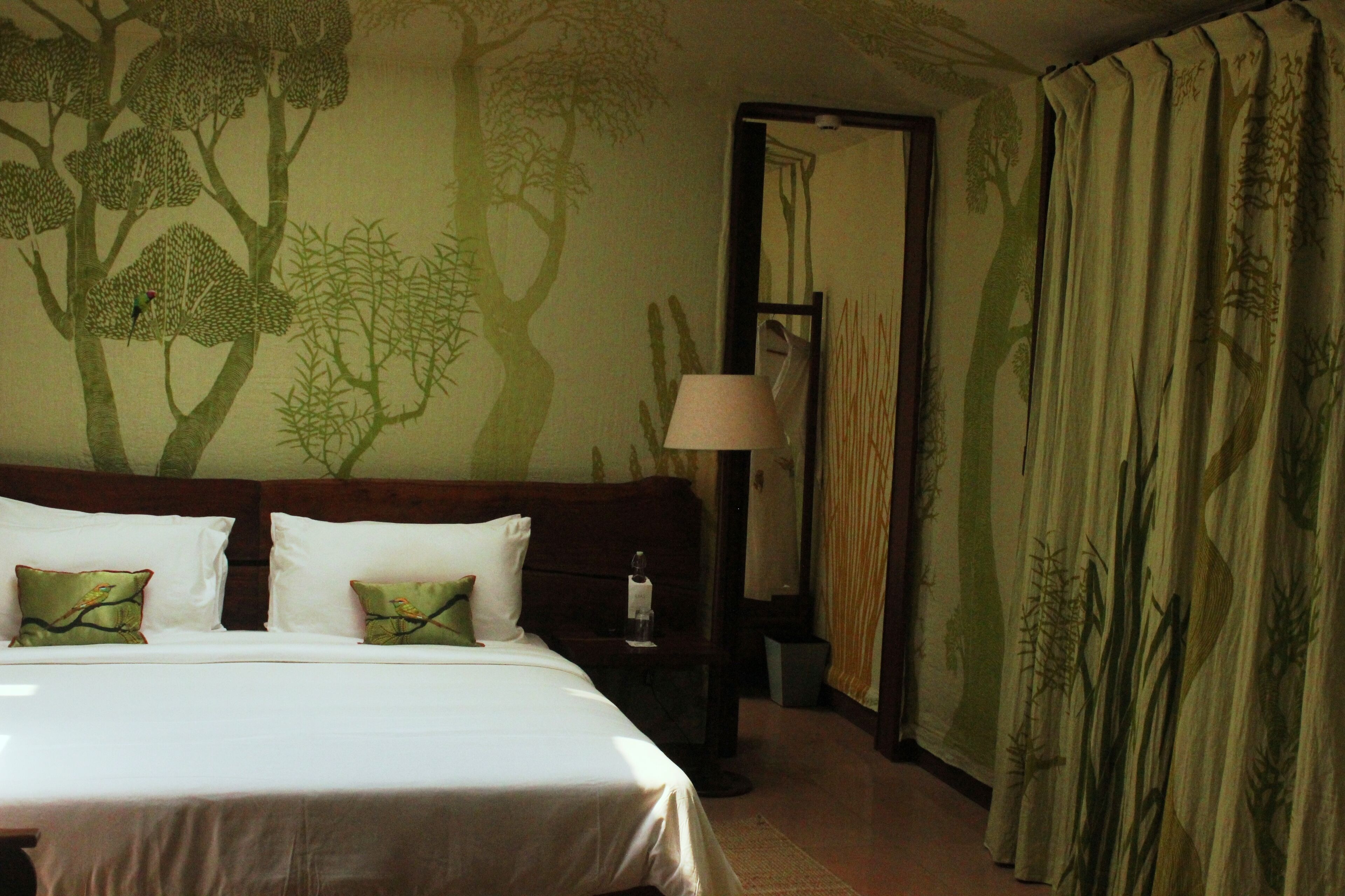 A hotel room with a large bed, a nightstand, a lamp, and a wall mural of trees.