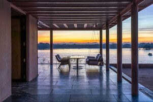 Un espacio de estar al aire libre techado con vista a un atardecer sobre el agua.