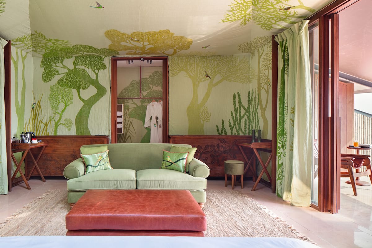Una habitación con un sofá verde, un pouf rojo y una mesita de madera.