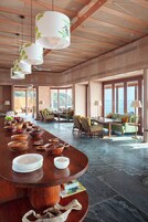 Un comedor amplio con una larga mesa de madera, rodeado de asientos cómodos y grandes ventanales con vistas al mar.