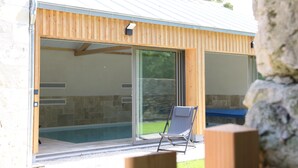 A modern outdoor pool area with a wooden deck, a lounge chair, and a stone wall. - Gite l'Hermine, 15 pers, heated indoor pool, RDC PMR, enclosed garden (Azay-le-Rideau)
