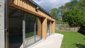 A modern building with large sliding glass doors, a stone wall, and a grassy yard. - Gite l'Hermine, 15 pers, heated indoor pool, RDC PMR, enclosed garden (Azay-le-Rideau)