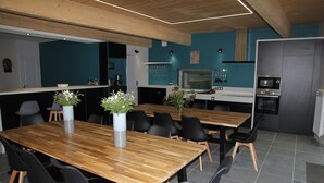 A modern kitchen with a microwave, oven, and coffee machine. There are two wooden tables with chairs, and a potted plant on each table. - Gite l'Hermine, 15 pers, heated indoor pool, RDC PMR, enclosed garden (Azay-le-Rideau)