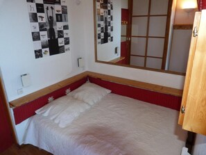 A single bed with a red headboard and white bedding in a small room with a wooden door and a mirror on the wall.