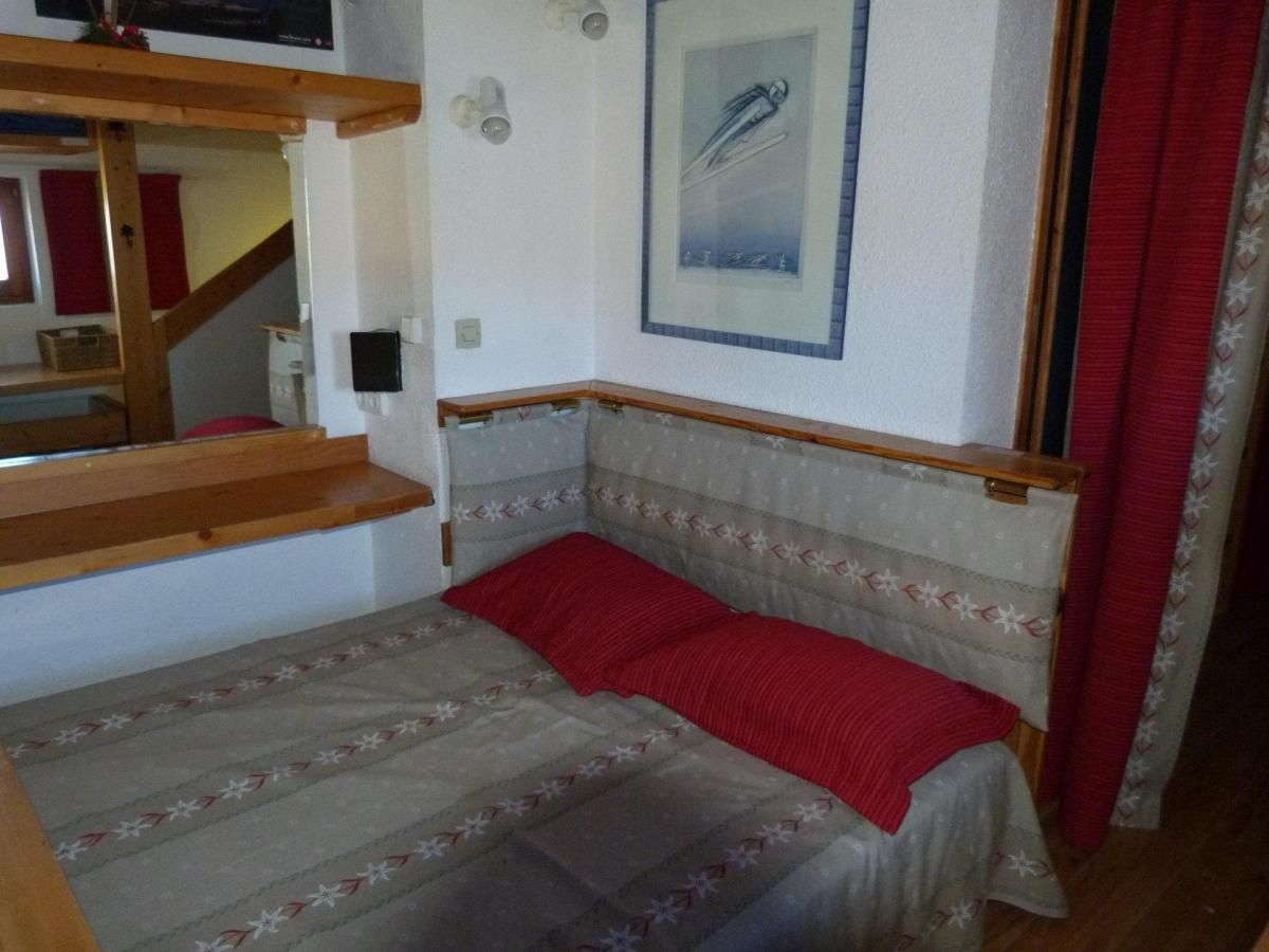 Ein kleiner, gemütlicher Raum mit einem Bett, einem Holzregal, einer Treppe und einem gerahmten Bild an der Wand.