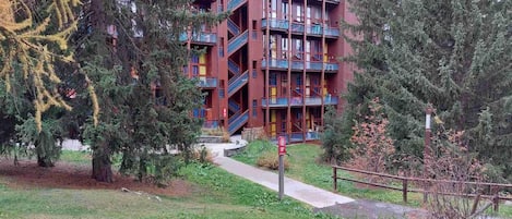 A multi-story building with balconies, surrounded by trees and a grassy area.