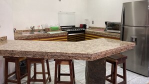 Una cocina con encimeras de granito, taburetes de madera, un refrigerador de acero inoxidable y una estufa a gas.