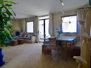 A spacious living area with a sofa, dining table, and chairs. There is a large window providing natural light and a view of the outdoors.