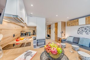 A modern kitchen with wooden accents, a dining area with a fruit bowl, and a living space with a sofa and wall art.