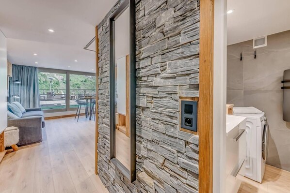 A modern interior with a stone wall, a visible bathroom with a washing machine, and a dining area with a view.