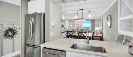 A modern kitchen with a stainless steel refrigerator, dishwasher, and marble countertop.