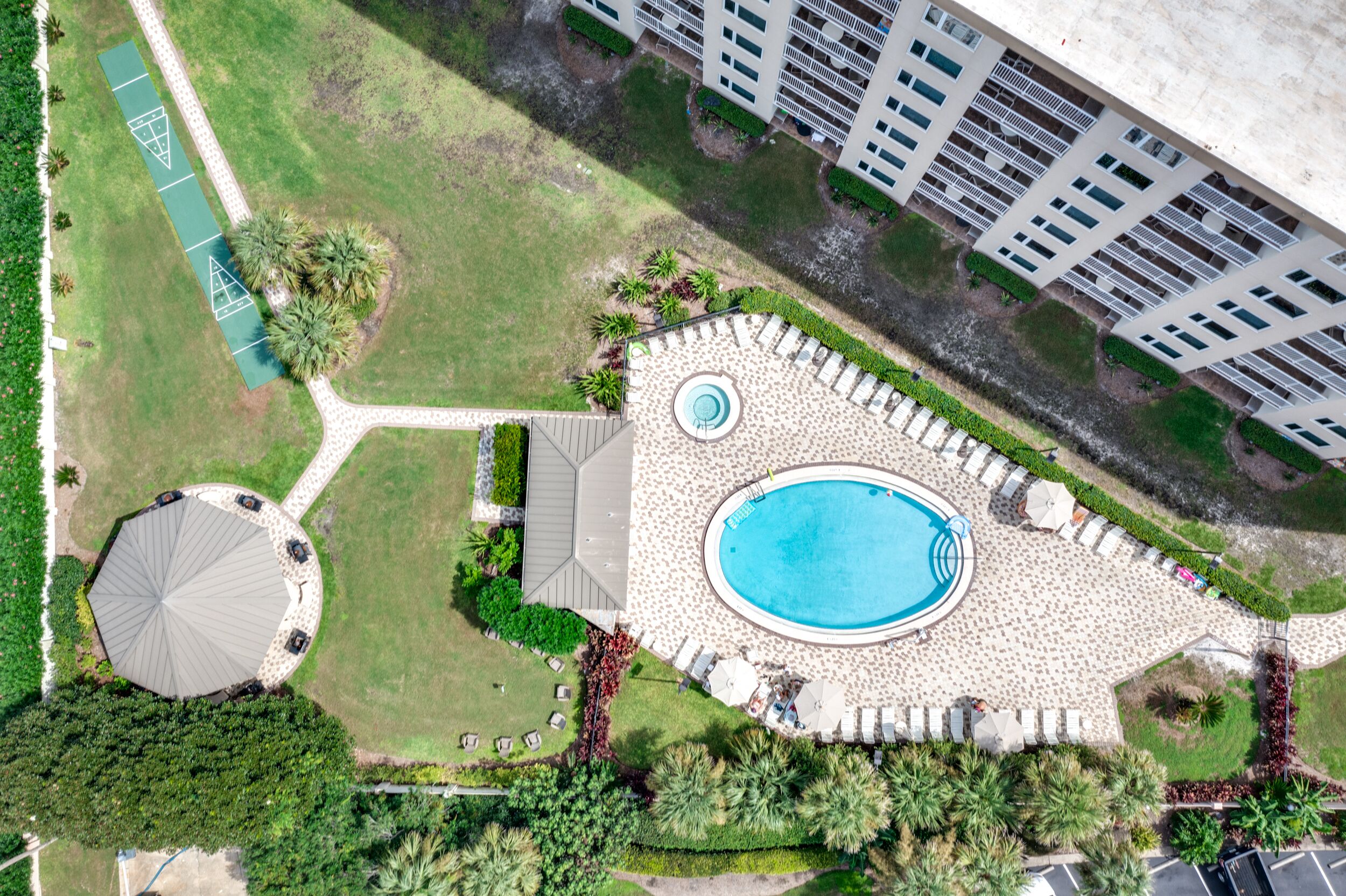 An aerial view of a resort with a swimming pool, a circular gazebo, and a tennis court.