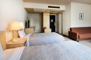 A hotel room with two beds, a desk with a lamp, a TV, and a brown sofa. - Hotel Sports Palko (Gifu)