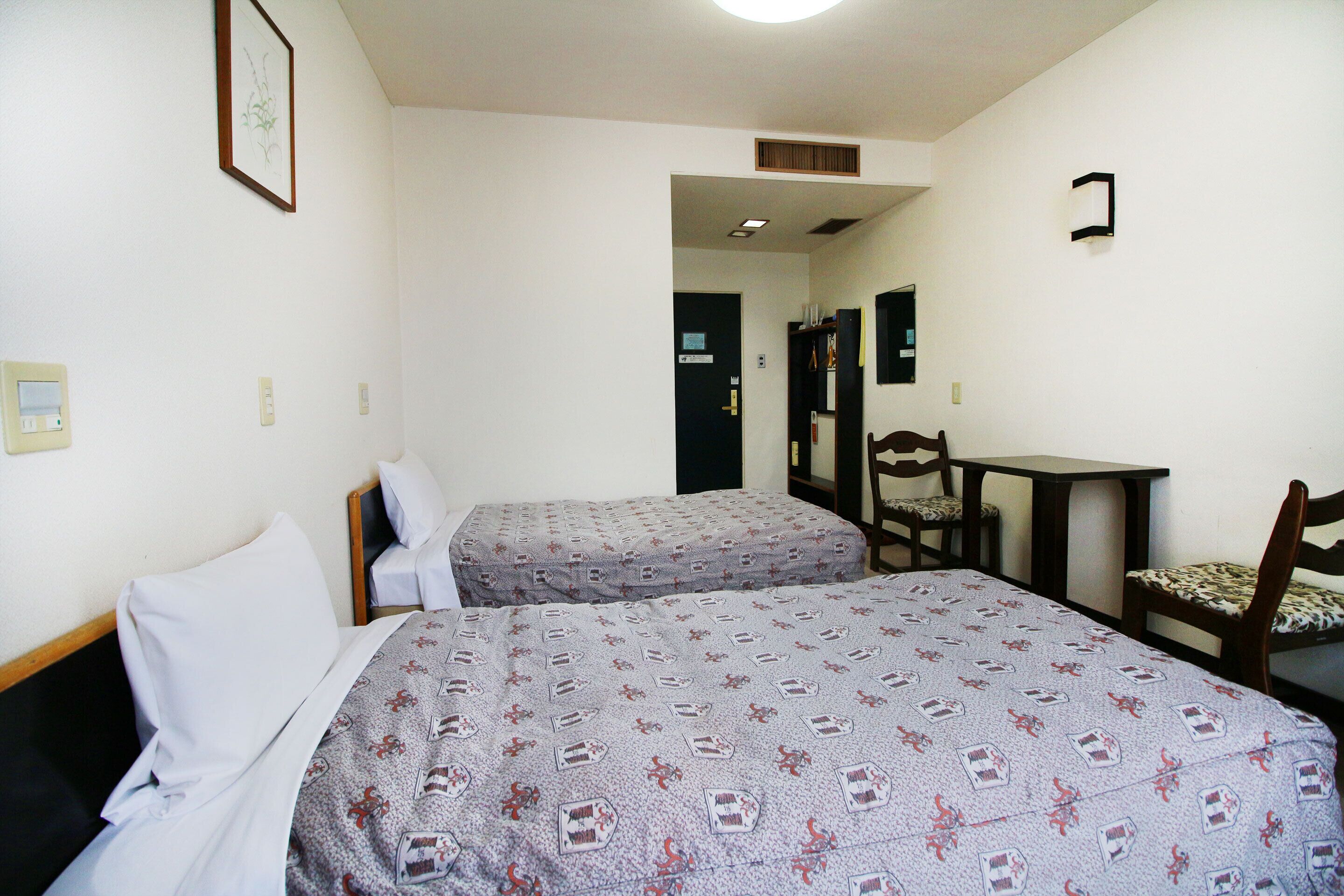 Une chambre d’hôtel avec deux lits simples, un bureau, une chaise et un miroir.
