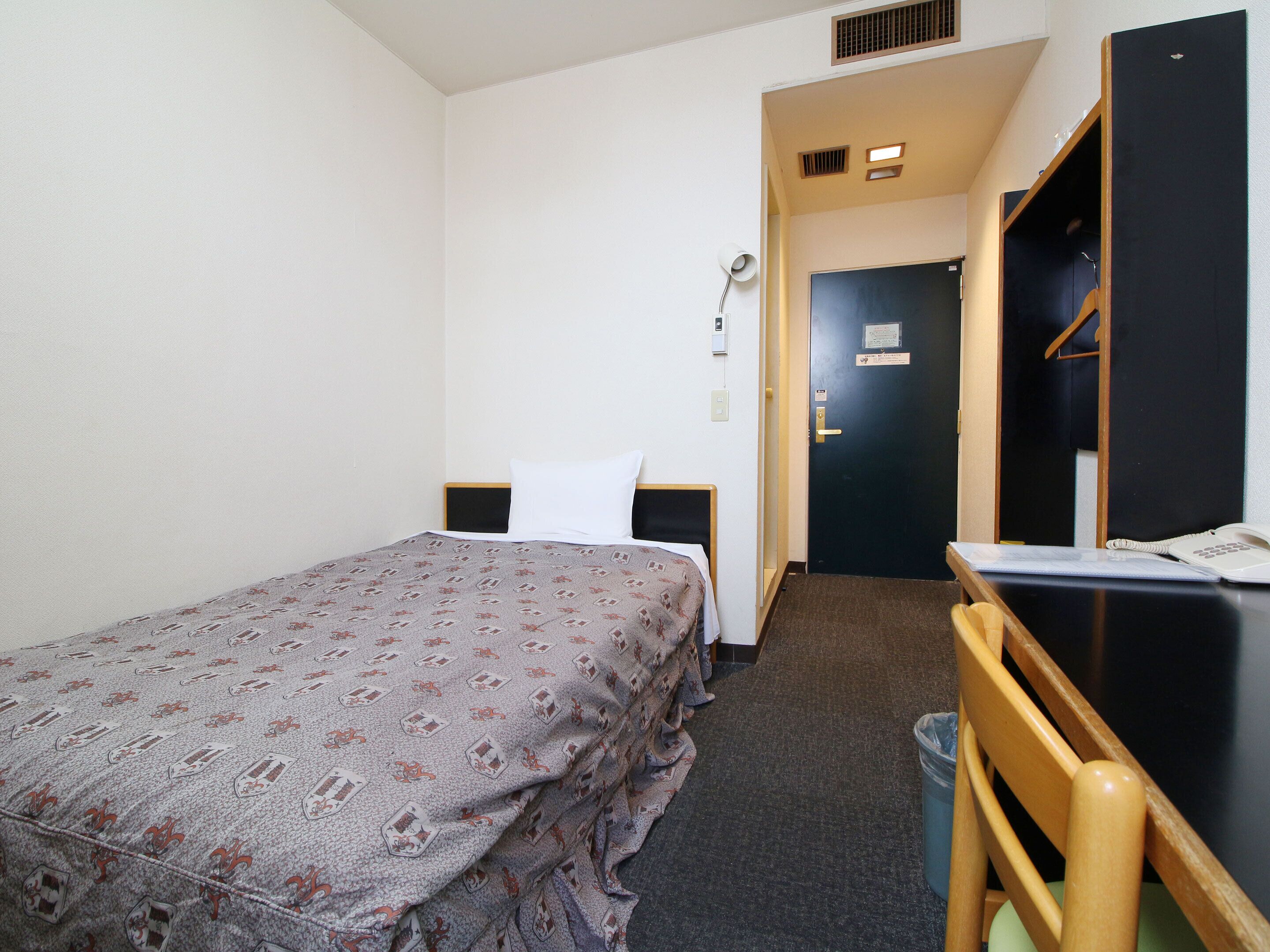 A hotel room with a bed, a desk with a telephone, and a wardrobe.