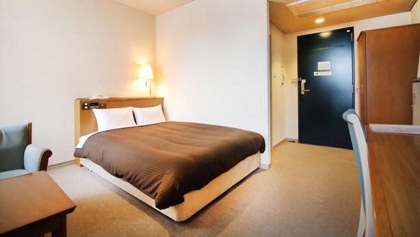 A hotel room with a bed, a desk, a chair, a lamp, and a door. - Hotel Sports Palko (Gifu)