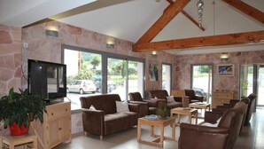A spacious living area with stone walls, wooden furniture, and large windows offering a view of parked cars outside. - Wifi, view mountain, swimming pool, sauna, hammam, terrace, balcony, parking, tv, ski locker, 38m² (Luz-Saint-Sauveur)