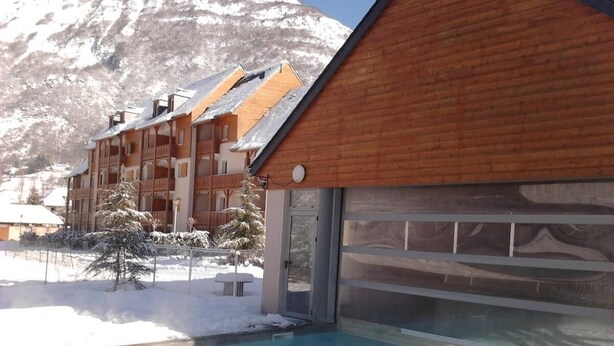 A wooden building with a pool, snow-covered trees, and mountains in the background. - Wifi, view mountain, swimming pool, sauna, hammam, terrace, balcony, parking, tv, ski locker, 38m² (Luz-Saint-Sauveur)