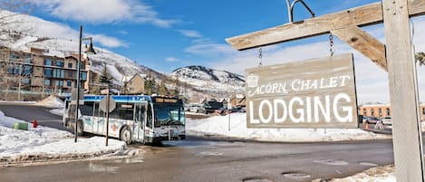 A bus at a stop with a sign for 'Acorn Chalet Lodging' in the background.