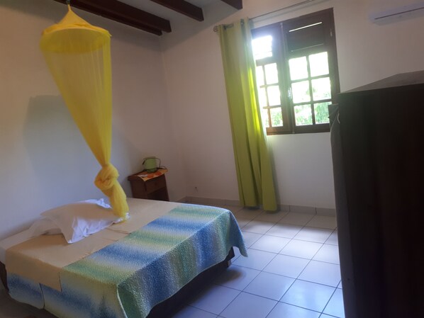A room with a bed, a window with curtains, a small table with a plant, and a yellow hanging canopy.