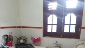 A kitchen with red cabinets, a white countertop, a stove, a sink, and a window with a view of the outside. - Charming cozy house type T3---------------------- (sainte-anne en Guadeloupe)