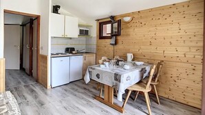A compact kitchen with white cabinets, a microwave, and a sink. A dining table with chairs is set against a wooden wall.