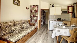 A cozy living room with a patterned sofa, a dining table with chairs, and a kitchen area with cabinets and appliances.