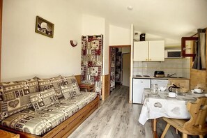 Een knus woongedeelte met een gestreept bankje, een eettafel met stoelen, en een keuken met kastjes en apparatuur.