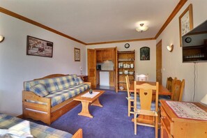 A cozy living room with a plaid sofa, wooden dining table, and chairs. There is a kitchen area with wooden cabinets and a refrigerator. - 10m from ski slopes, 6th floor, balcony, 40m², Méribel-Mottaret (Méribel - Les Allues)