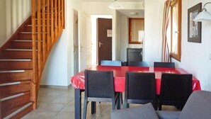 A dining area with a red table and black chairs, a staircase with wooden railings, and a kitchen in the background.