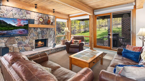 Ein gemütliches Wohnzimmer mit Kamin aus Stein, Ledersofas und einem großen Fenster mit Blick ins Freie.