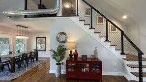 A spacious living area with a dining table, chairs, a red cabinet, a staircase, and a large window. - Close to town Large Yard Fire Pit Gas Grill Beach 2.5 blocks (Union Pier)