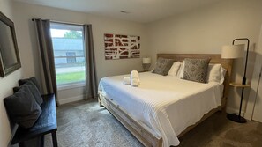 A hotel room with a bed, a bench, a bedside table, a lamp, and a window with curtains. - Close to town Large Yard Fire Pit Gas Grill Beach 2.5 blocks (Union Pier)