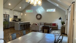 Une cuisine spacieuse avec un îlot central, un coin repas avec une grande table et un salon confortable avec un canapé et une horloge au mur.