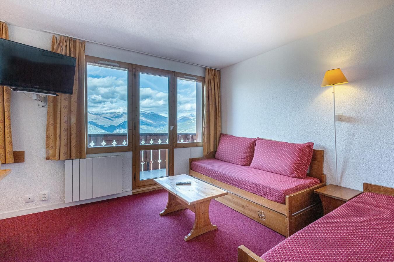 Ett rum med en soffa, ett litet bord, en tv och ett fönster med utsikt över bergen.