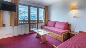 Une pièce comprenant un canapé, une petite table, un téléviseur et une fenêtre donnant sur la montagne.
