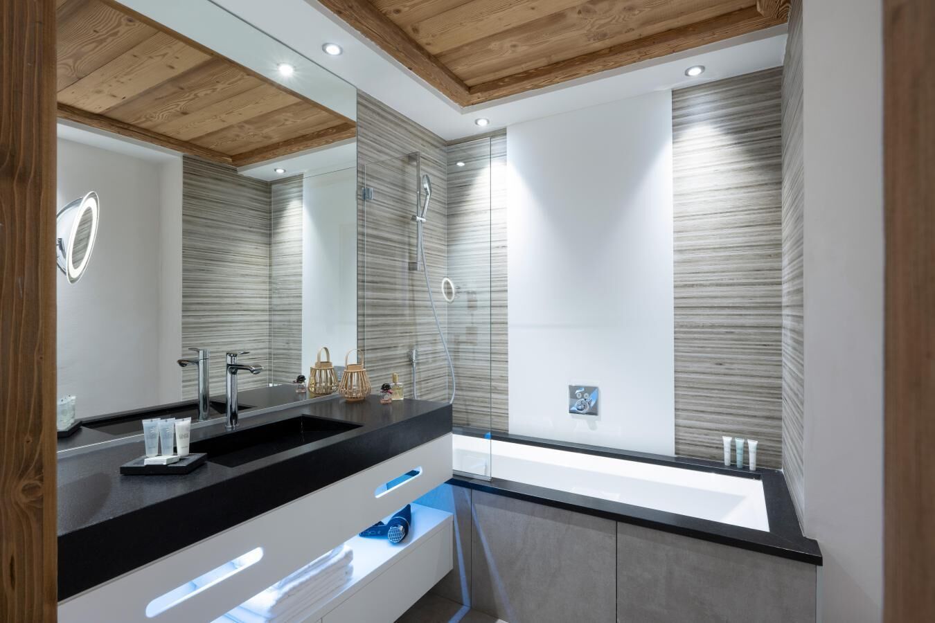Une salle de bain moderne avec un grand miroir, un plan de toilette noir, un lavabo intégré et une zone de douche séparée.