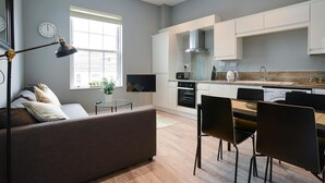A modern kitchen with white cabinets, a dining area with black chairs, and a grey sofa. - Arena Apartments (Nottingham)